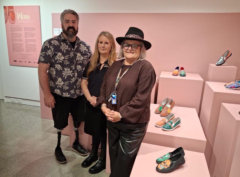 Neil Wallace, Sharon Hall and Gilli Marshall at the opening of Worn. They are standing in front of a display of the artworks.